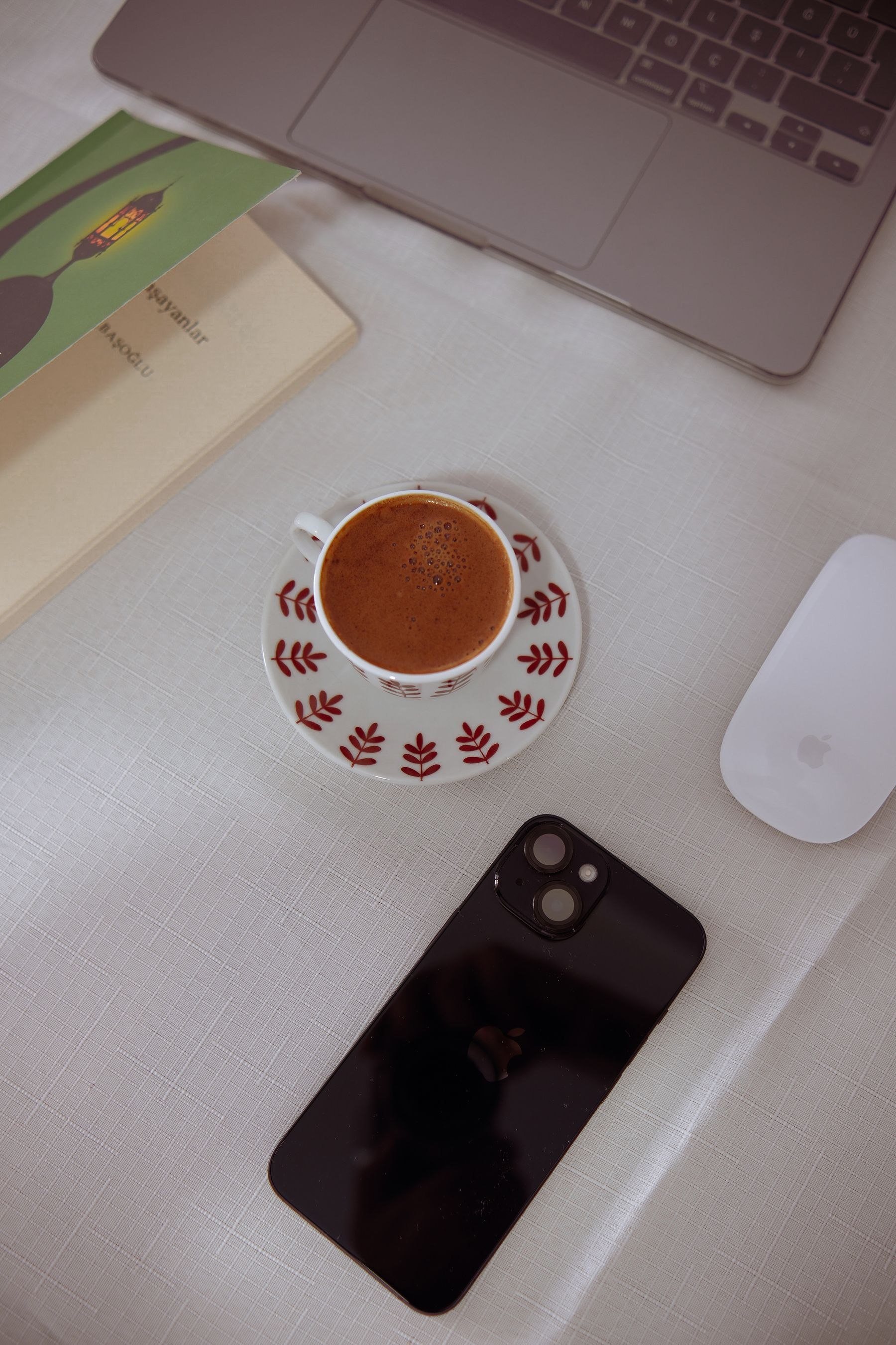 A phone and laptop on a desk, next to a coffee